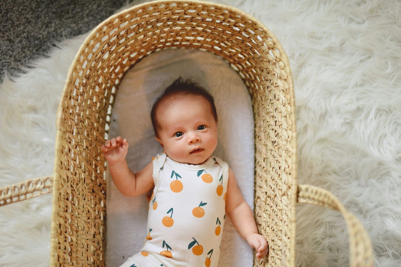 Newborn baby lying in a wicker moses basket on a sheepskin rug